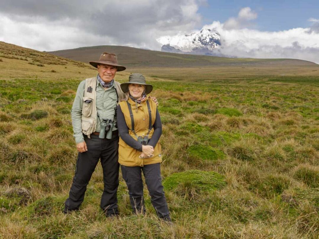 Norby Lopez and Susy Muñoz stand together on the Andean páramo with Antisana volcano behind them under a partly cloudy sky.